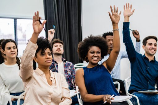 Group of young people sitting on conference together while raising their hands to ask a question. Business team meeting seminar training concept.